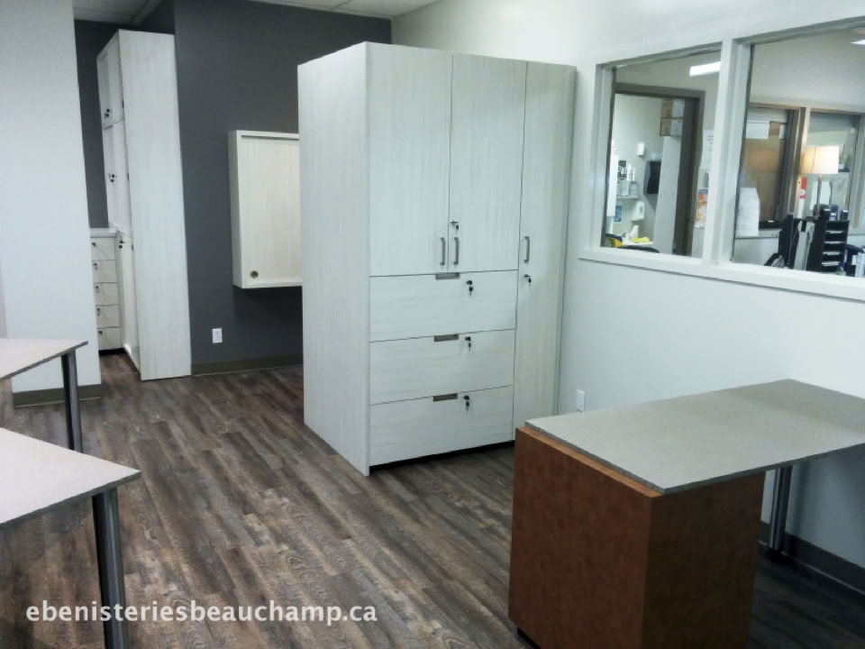 Office space with wooden flooring, a large white cabinet, desks, and windows with a view into another room.