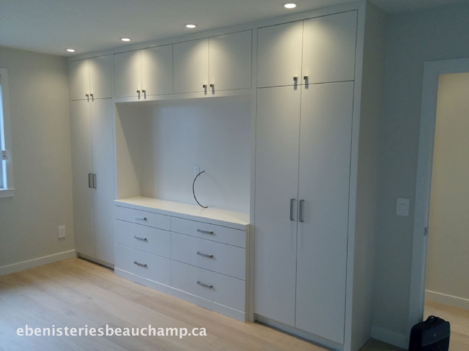 Placard encastré blanc avec plusieurs portes et tiroirs, éclairage encastré au plafond.