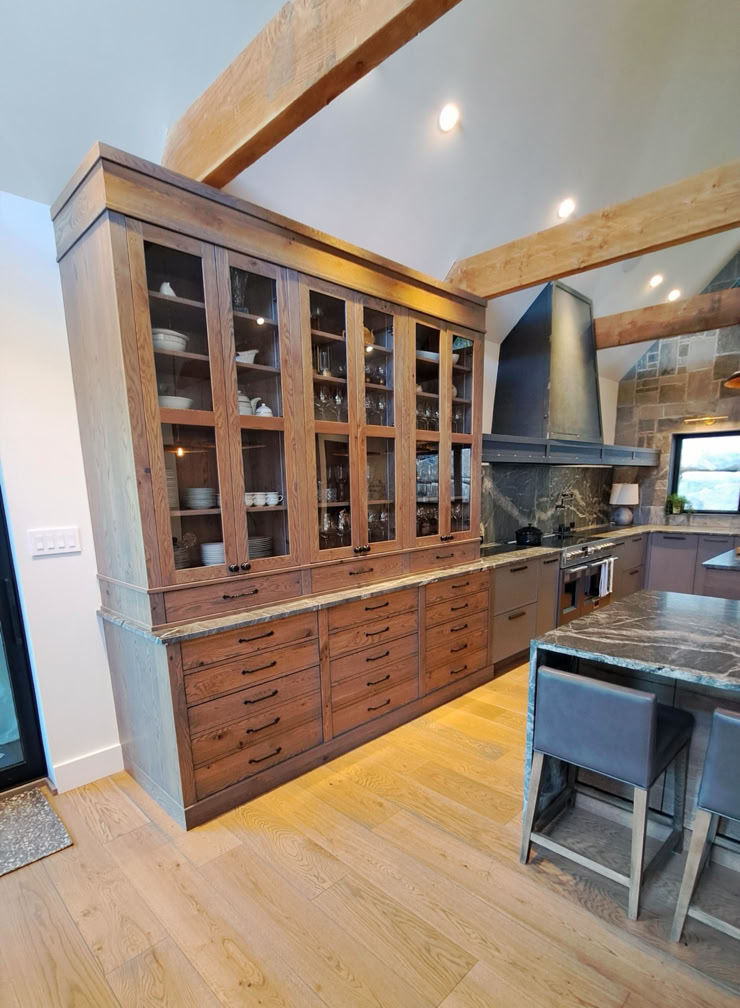 A kitchen with wooden cabinets, glass-fronted upper cupboards, a black range hood, and a kitchen island with bar stools.