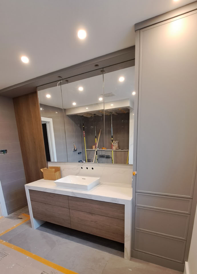 Salle de bain moderne avec un grand miroir, un lavabo rectangulaire sur un meuble en bois, et des lumières encastrées au plafond.