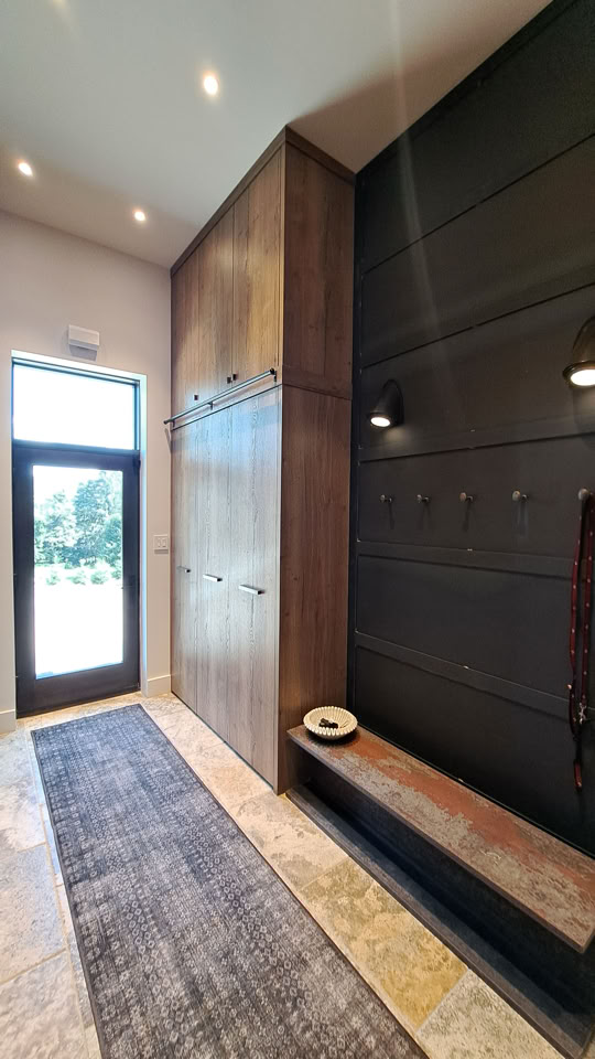 Entrée moderne avec un grand placard en bois à gauche, un banc avec des crochets au-dessus à droite, un tapis au sol et une porte vitrée au fond.