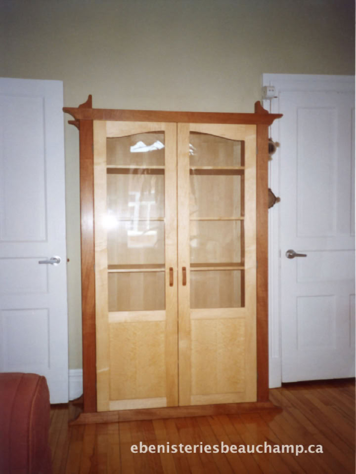 Armoire en bois avec portes vitrées, située entre deux portes blanches dans une pièce.