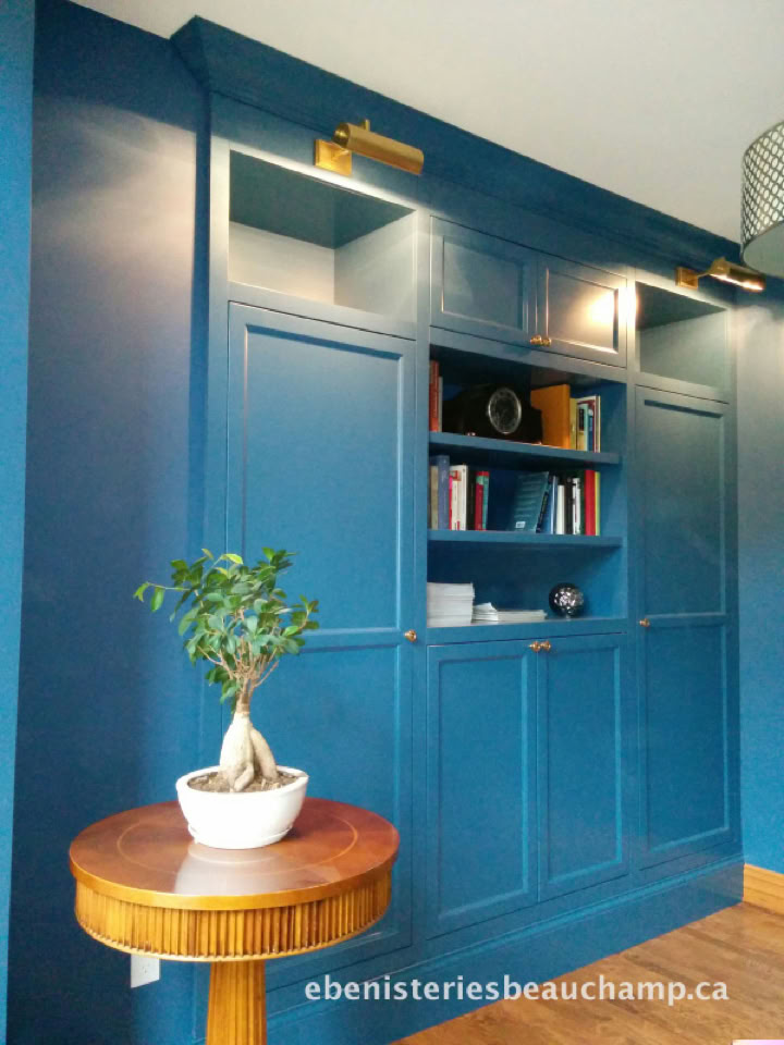 Armoire murale bleue avec étagères ouvertes contenant des livres et des objets décoratifs, petite table ronde en bois avec une plante en pot.