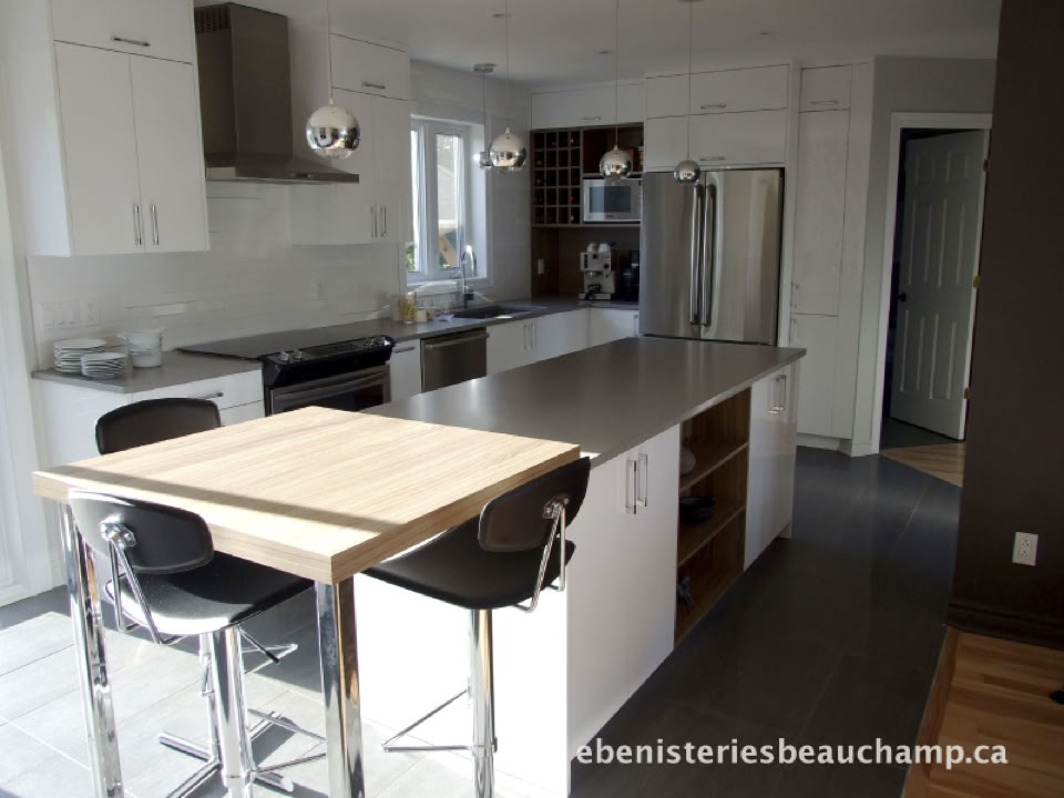 Cuisine moderne avec un îlot central, des armoires blanches, un réfrigérateur en acier inoxydable, et une table en bois avec deux chaises noires.