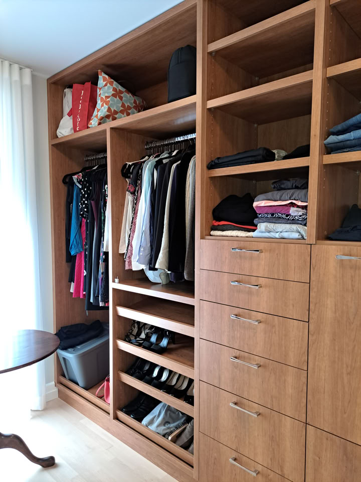 Armoire en bois avec vêtements suspendus, étagères contenant des sacs et des vêtements pliés, et tiroirs en bas.