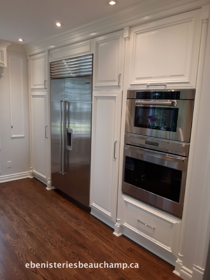 Cuisine moderne avec réfrigérateur en acier inoxydable encastré, fours intégrés et plancher en bois.