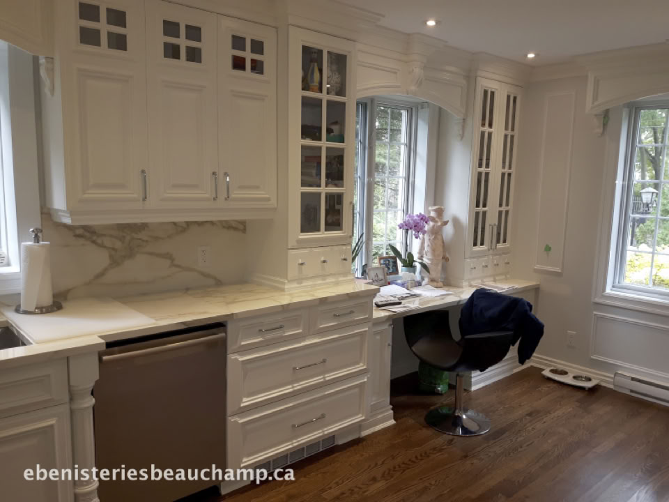 Cuisine moderne avec armoires blanches, plan de travail en marbre, chaise de bureau noire, et fenêtre donnant sur l'extérieur.