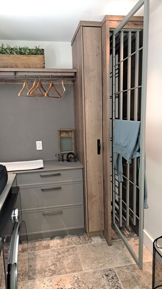Buanderie avec des armoires grises, un comptoir, des cintres en bois, et une cage métallique avec une serviette bleue accrochée.