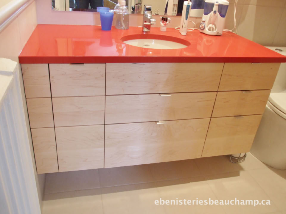 Meuble-lavabo en bois clair avec un plan de travail rouge, contenant divers articles de toilette et un évier intégré.