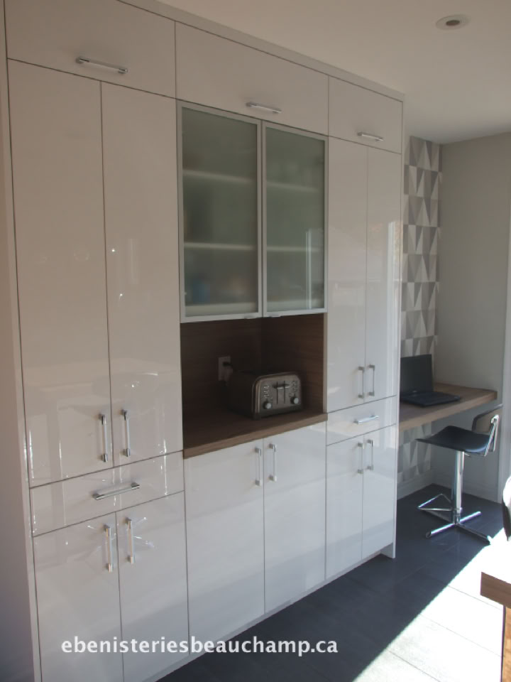 Placard de cuisine blanc avec des portes vitrées au centre, un espace ouvert avec un grille-pain, et un bureau avec une chaise à droite.