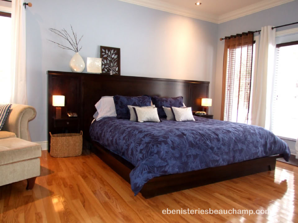 Chambre avec un grand lit à couverture bleue, deux lampes de chevet, un canapé beige, et un sol en bois.