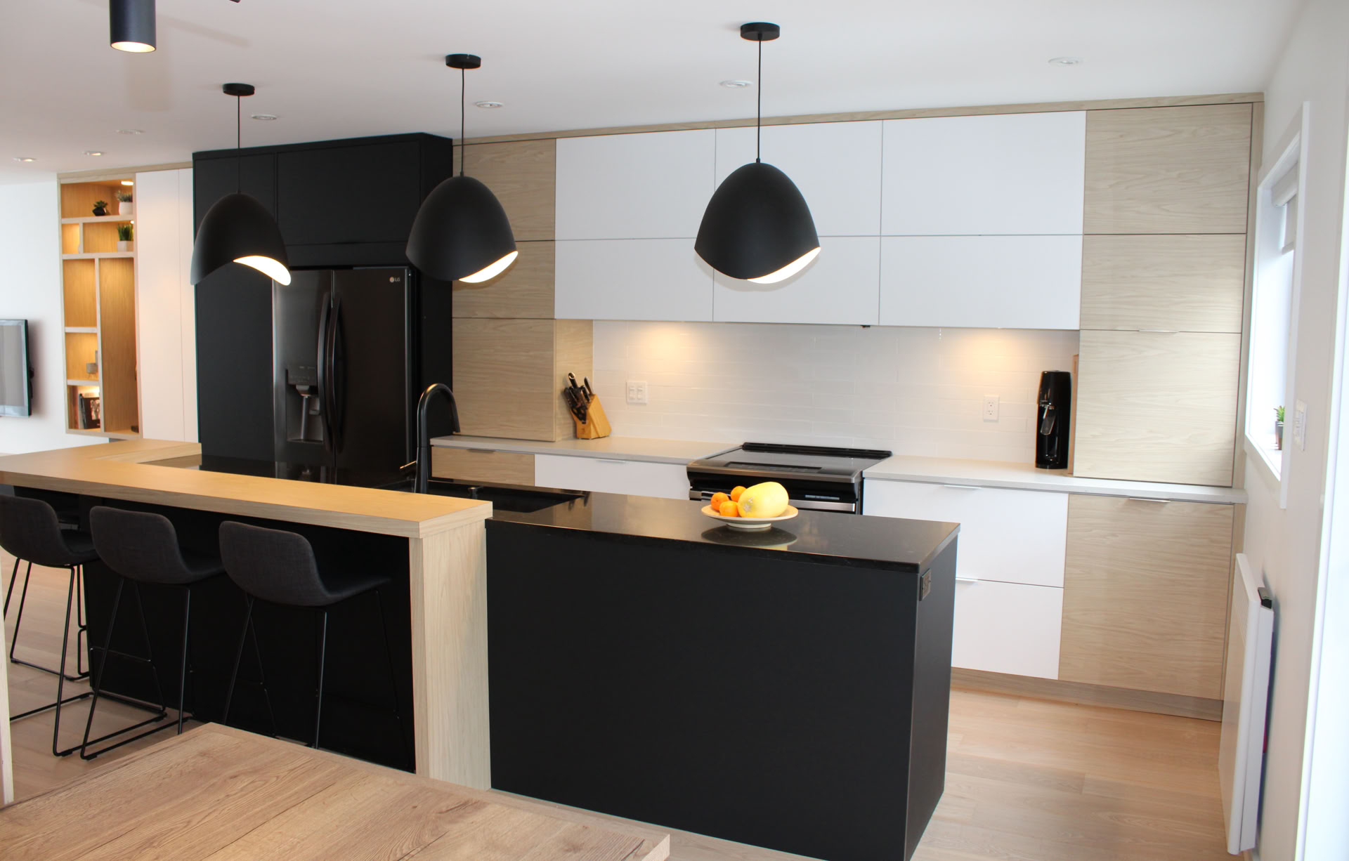 Cuisine moderne avec des armoires blanches, un îlot central noir, trois suspensions noires, et des tabourets noirs.