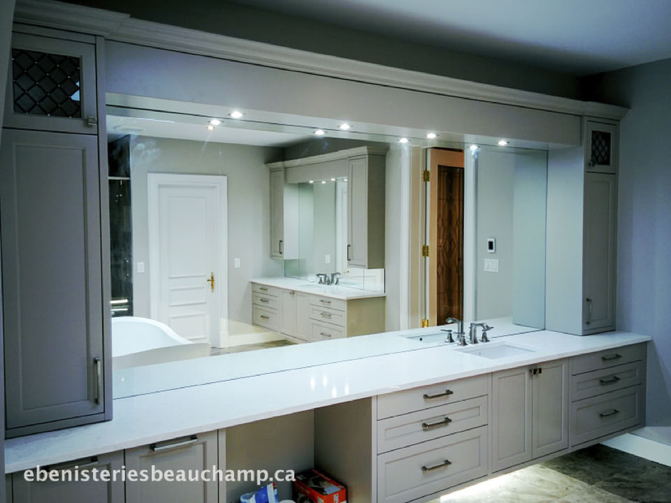 Salle de bain moderne avec un grand miroir, un comptoir blanc, des armoires grises et un évier intégré.