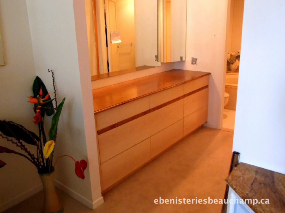 Commode en bois clair avec un miroir au-dessus, située dans un couloir avec un vase de fleurs colorées à gauche.