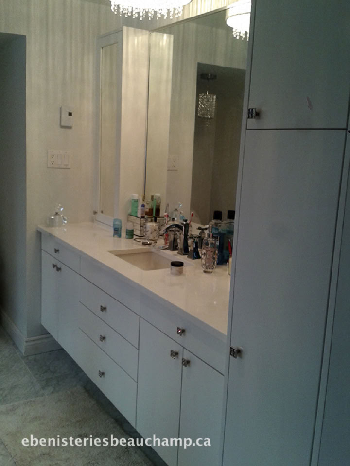Salle de bain avec un grand miroir, un lavabo, des produits de toilette sur le comptoir, et des armoires blanches.