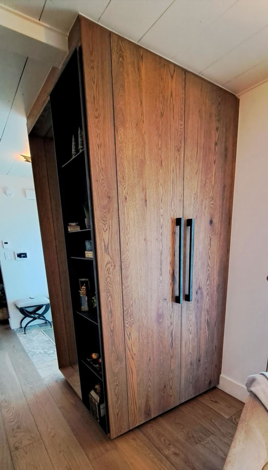 Armoire en bois avec deux grandes poignées noires, située dans une pièce avec un sol en bois.