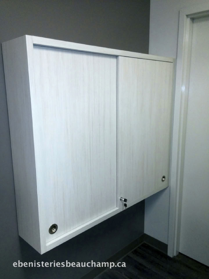 Armoire murale blanche avec deux portes coulissantes dans une pièce aux murs gris.