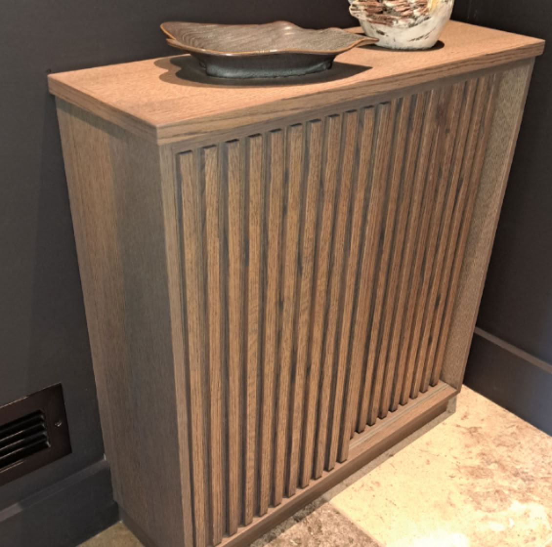 Meuble en bois avec des rainures verticales, surmonté de deux objets décoratifs.