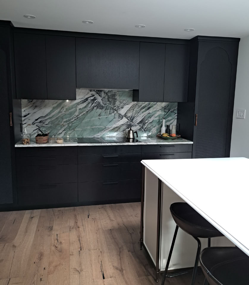 Cuisine moderne avec des armoires noires, un dosseret en marbre, un plan de travail blanc et des tabourets noirs.